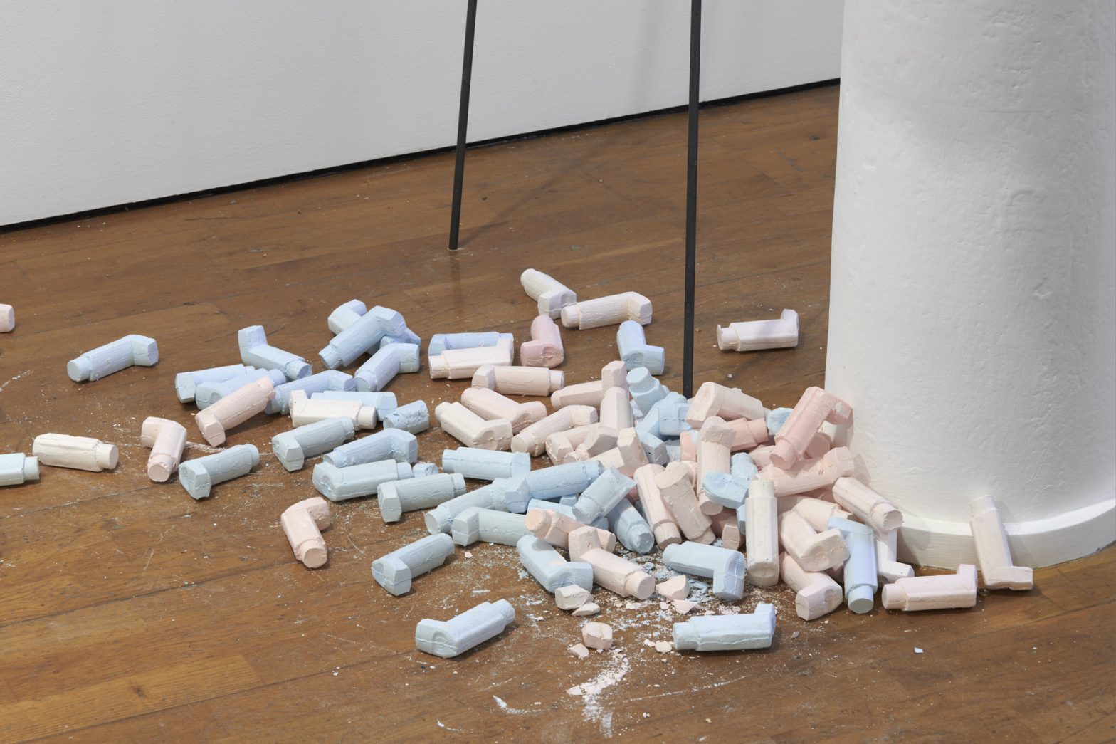 Soft pink and blue coloured asthma inhalers cast in plaster in a pile on a wooden floor, some of them broken up.