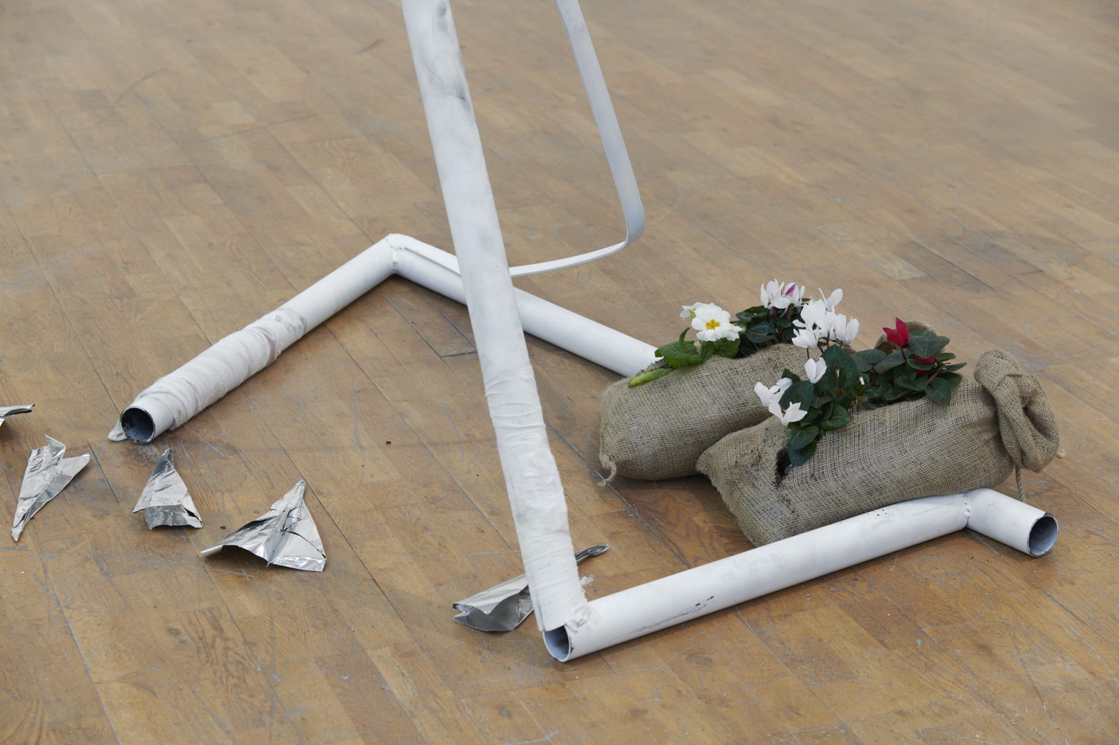 Two steel poles and two canvas bags containing brightly coloured flowers. Next to them are a scattering of tinfoil aeroplanes.
