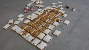Photo of lots of peanut butter and jam sandwiches laid out in rows on a concrete floor. The silhouette of a witch with a pointy hat has been superimposed onto the sandwiches.