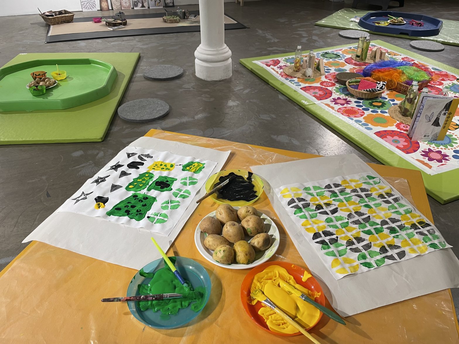 Brightly coloured potato prints laid out on the floor next to three bowls filled with paint and potatoes.