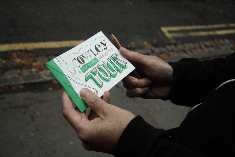 Two hands holding a small paper booklet entitled Cowley: A Self Guided Reflective Tour and a pencil.