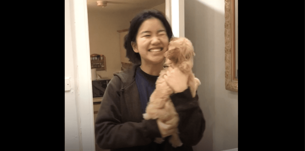 A young woman laughs holding a small golden puppy