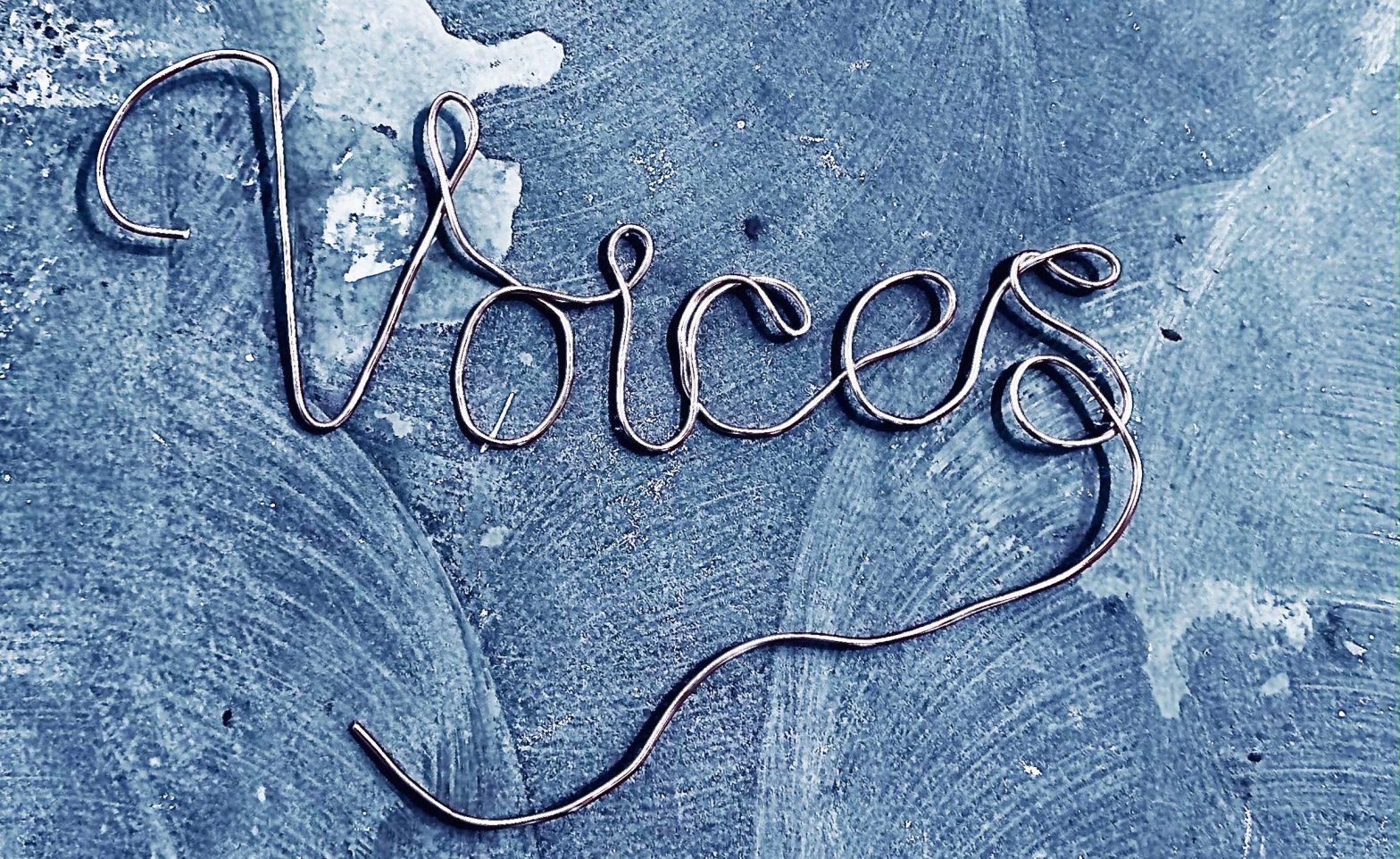 The word Voices made from wire against a floor or surface with patches of brushwork and watermarks.