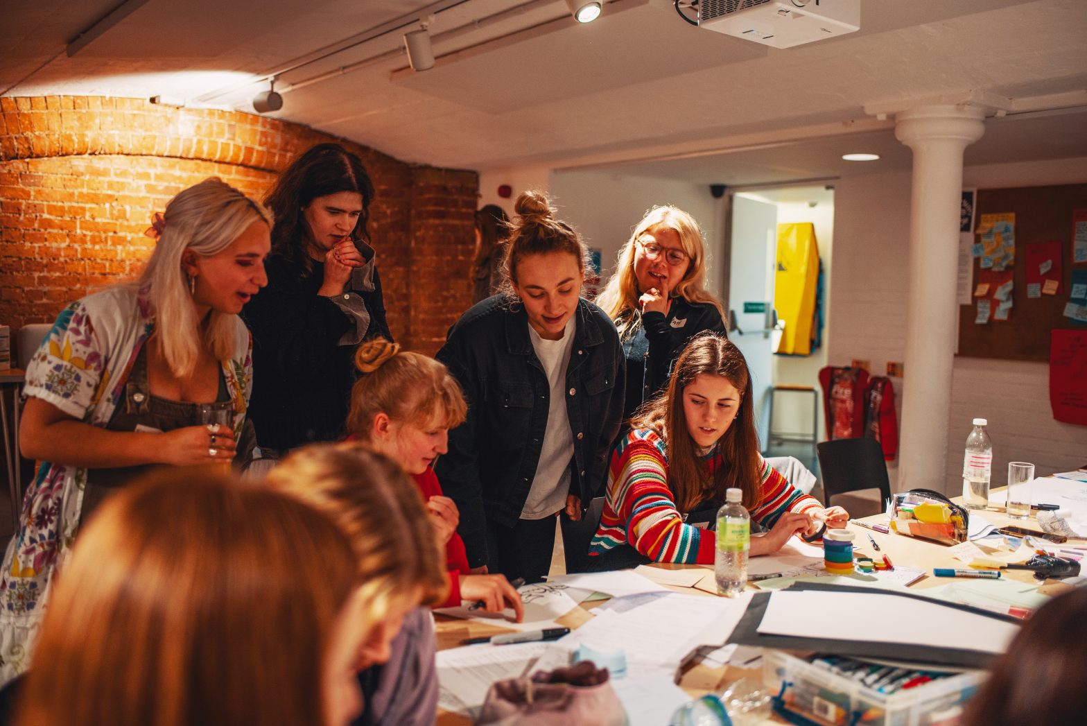 A group of people gathered round a table in Modern Art Oxford's Creative Space looking at artwork.