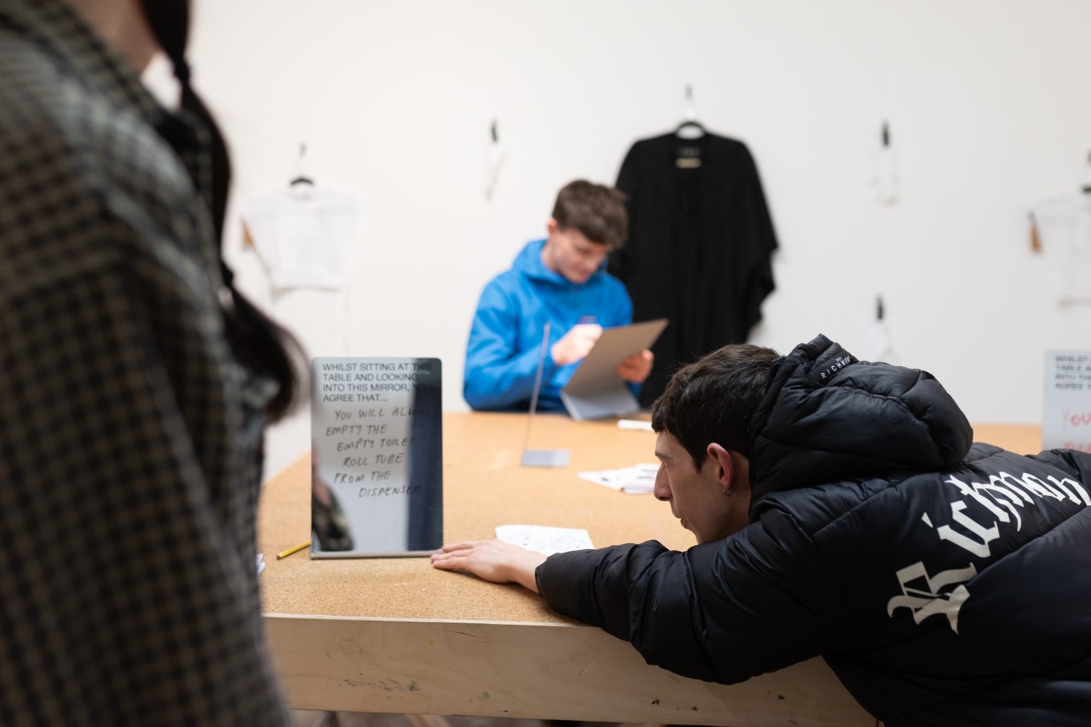 A man reaches over a table in Modern Art Oxford's Creative Space to read a mirror that has writing on it.