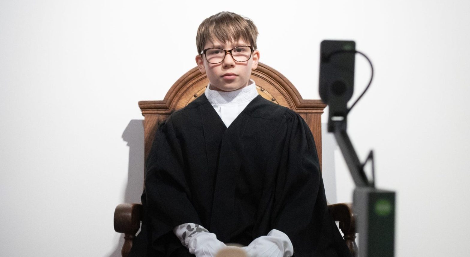 Young child sitting in a judges chair wearing judicial robes.