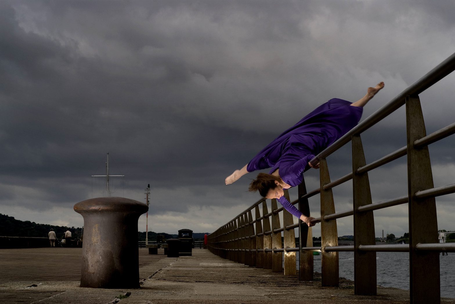 A woman dancing, holding herself upside down on a railing with her legs split in mid air.