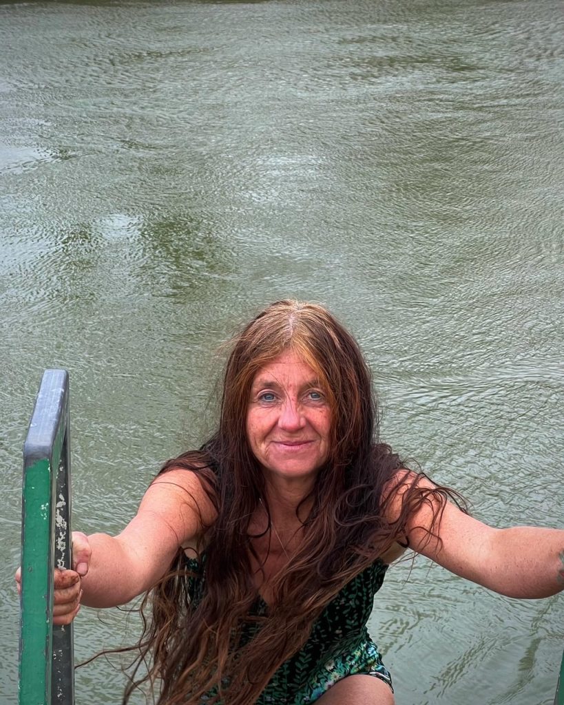 Helen Edwards emerges from a body of water with long hair spread over her shoulders. 