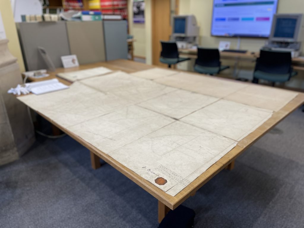 A large and ancient map laid out on a table showing areas of land including common ground. 