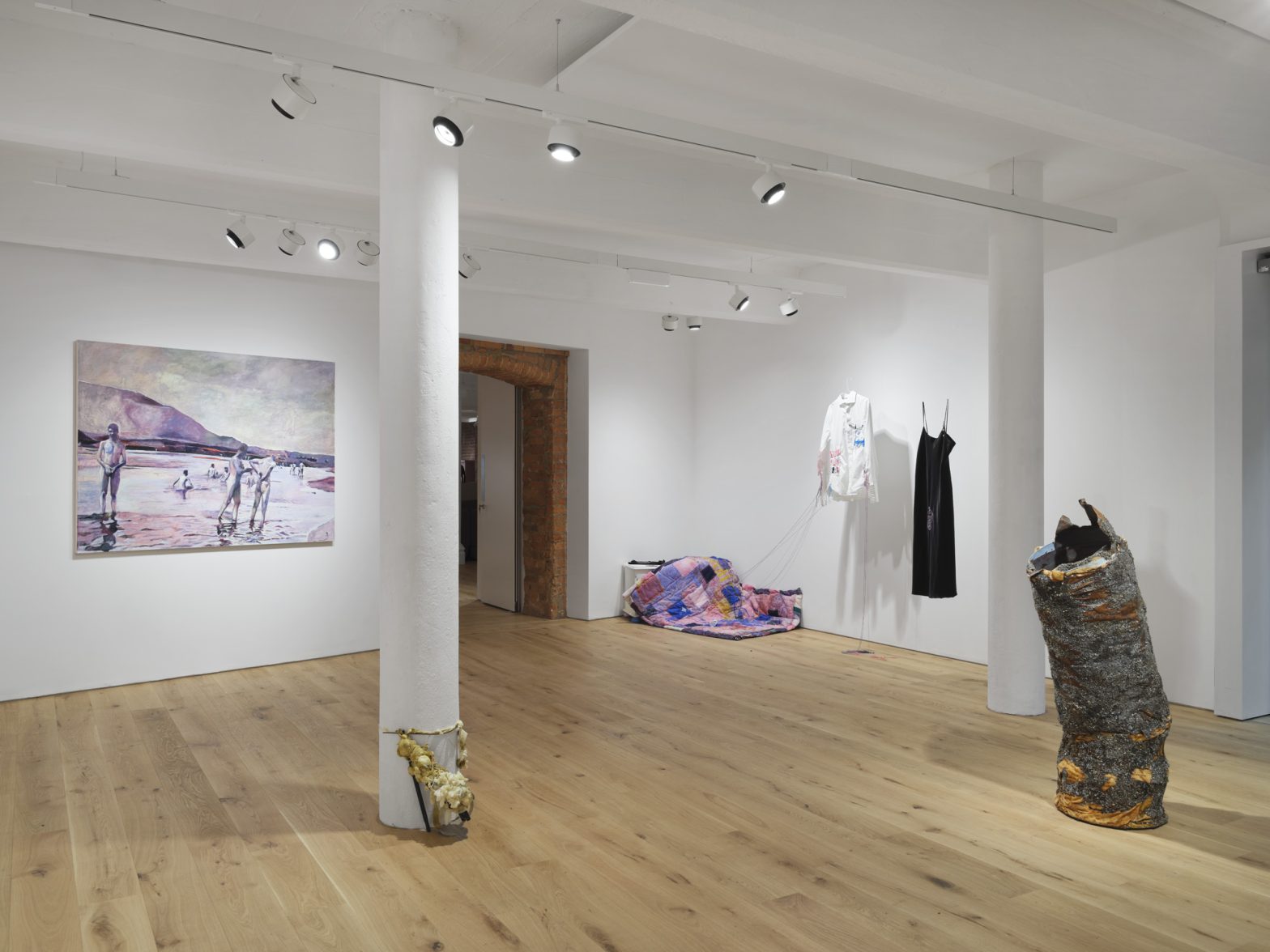 An installation view of a group exhibition showing a large painting, embroidered fabric and sculpture.