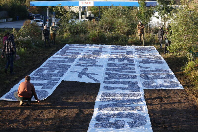 A large banner lies on the ground, with its text only partially legible. A man crouches beside it. 