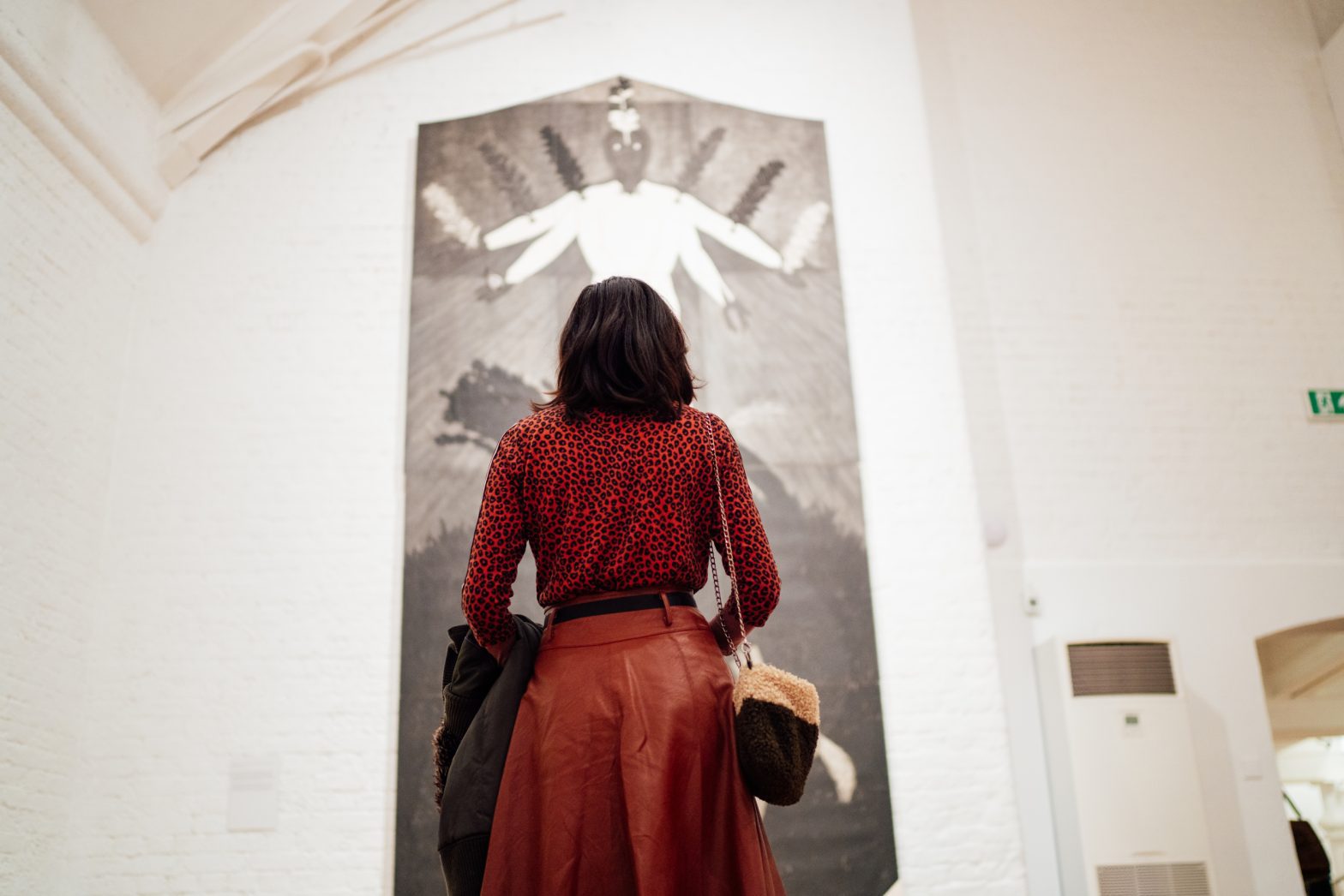 A photo of a woman standing in Modern Art Oxford's gallery looking at huge collography print by Belkis Ayón. She is wearing a red skirt and red top.