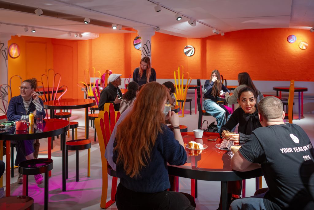 Visitors gather with cake and drinks in the brightly coloured Modern Art Oxford Café.