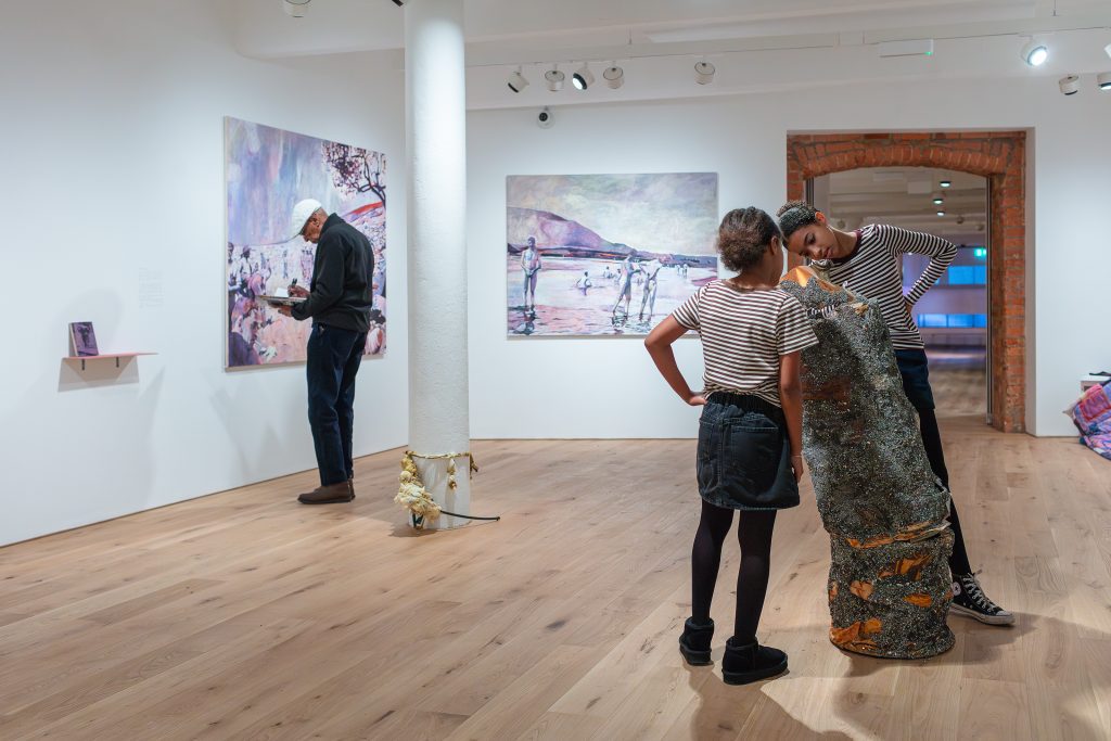 Two children examine a sculpture closely in a brightly lit gallery.